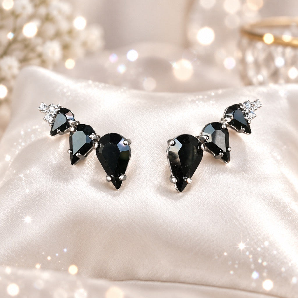 Zwarte oorstekers met drie druppelvormige Swarovski kristallen en zilverkleurige accenten op witte stof, statement oorbellen van DAMICE Jewelry